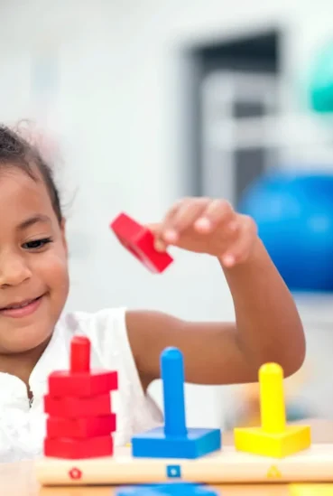Criança com terapeuta ocupacional brincando com blocos coloridos para desenvolver coordenação motora e habilidades funcionais.
